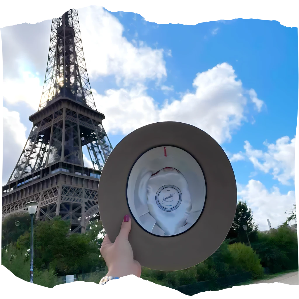 Hand holding a stylish hat with Agnoulita Hats logo against the backdrop of the Eiffel Tower in Paris.