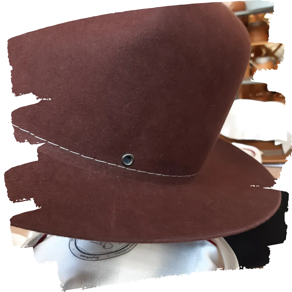 Close-up of a dark brown felt hat featuring a side grommet and white stitching detail, showcased on a hat stand