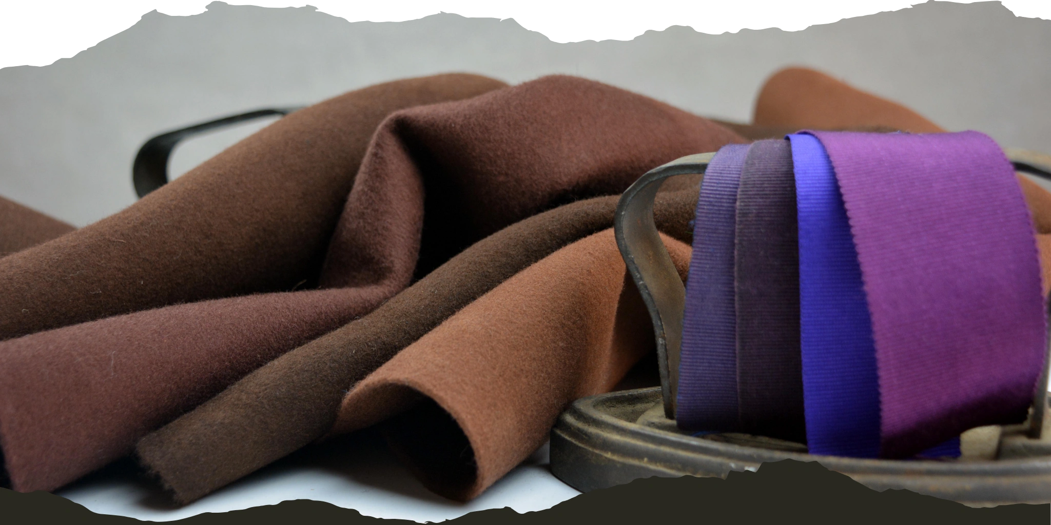 Assorted hat materials displayed, including rich brown and tan wool felts and a purple ribbon, emphasizing the variety of textures and colors