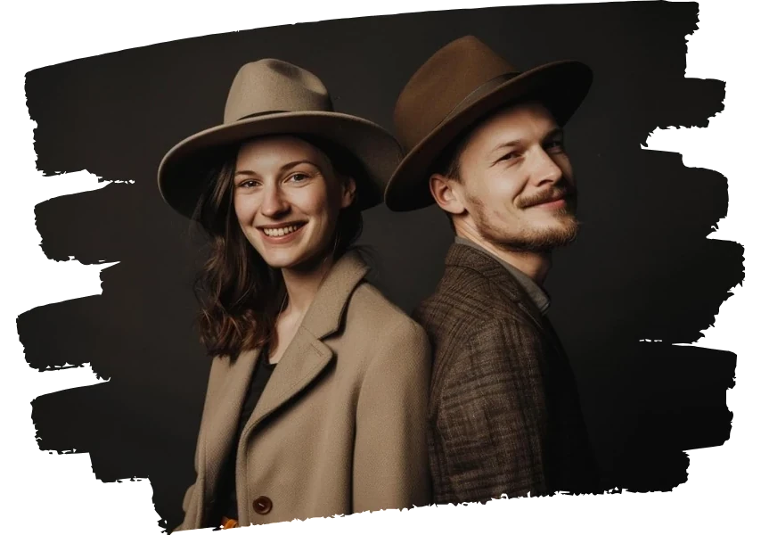 A stylish couple smiling while wearing custom Agnoulita hats, showcasing elegant fedora designs in neutral colors, perfect for a sophisticated outdoor ensemble.